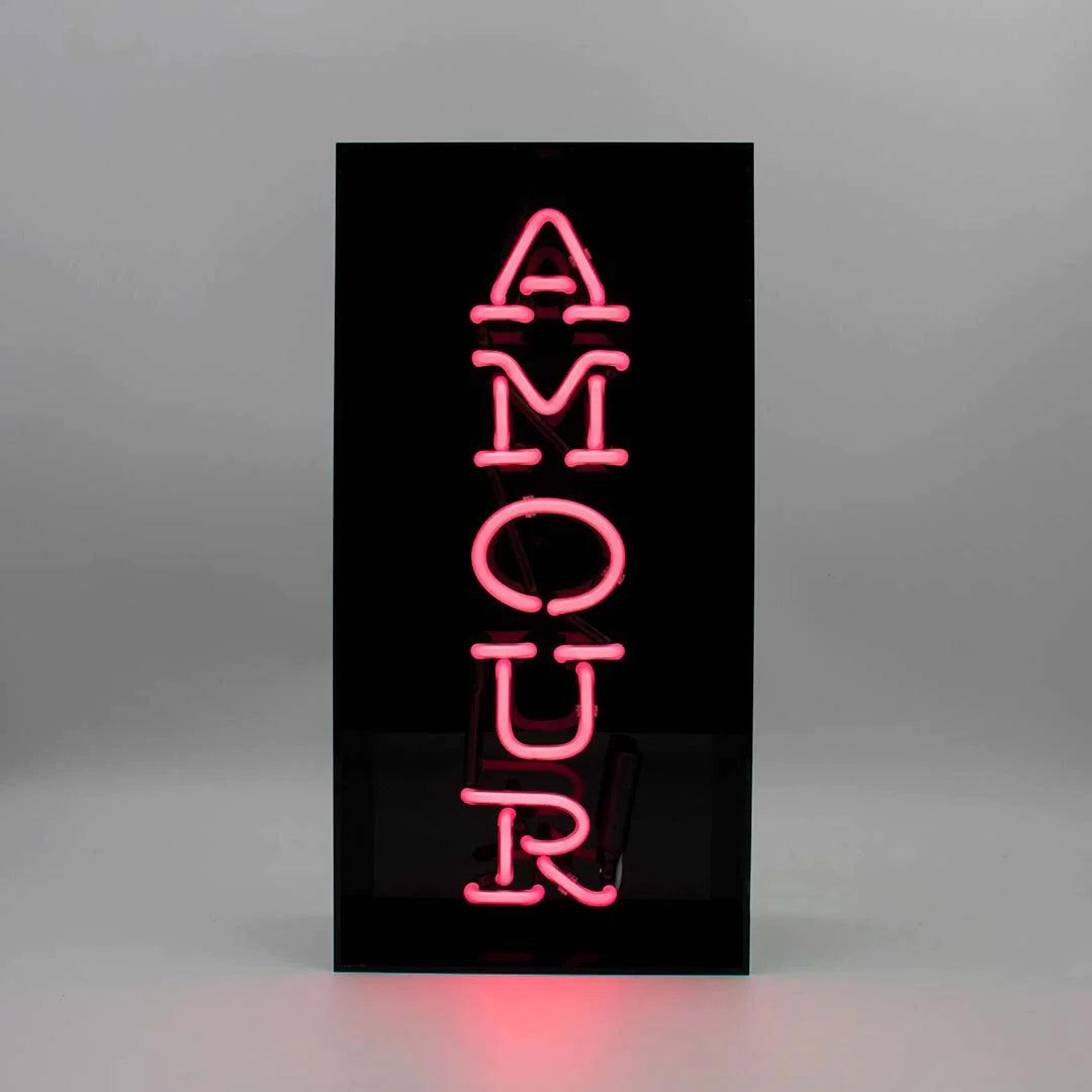TOM NEON Glas Neon Box 'Amour'. Stilvolle Neonbeleuchtung mit dem Wort 'Amour' in einer eleganten Glasbox. Perfekt für eine romantische und moderne Raumdekoration.
